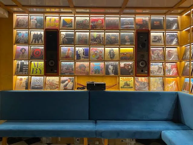 Parete di copertine di vinili retroilluminate con le casse, sopra i divanetti blu