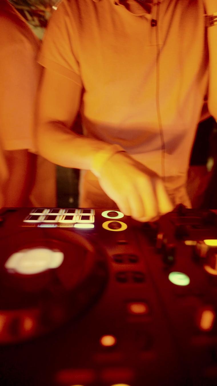 Mani del DJ sulla consolle illuminata durante un evento REWIND
